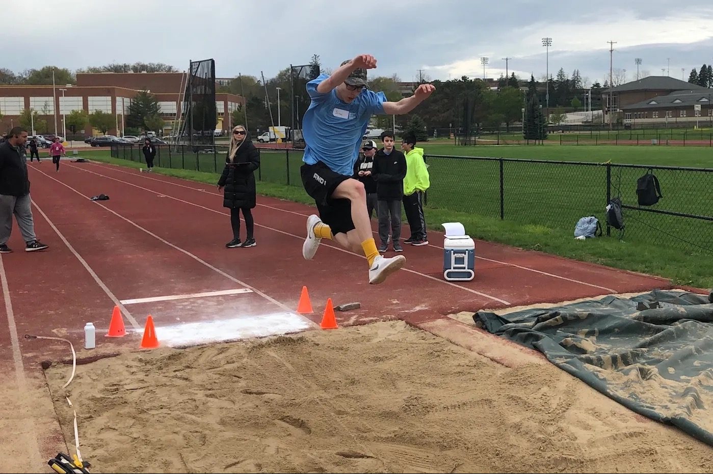 Sports Camp Athlete mid-air lunging over the sandpit during a long jump competition with several spectators 